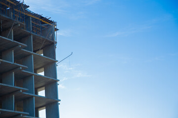 A partially constructed concrete building on the construction site with scaffolding and a bright blue sky, highlighting architectural progress and development. The concept of construction of an