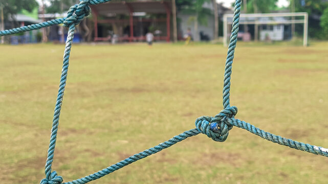 Close-up view of the goal net with intertwined knots. Soccer goal background with defocused green field.