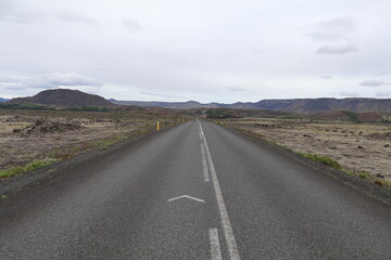 long straight road in Iceland through moss covered lavafields leading towards a mountain range in the distance