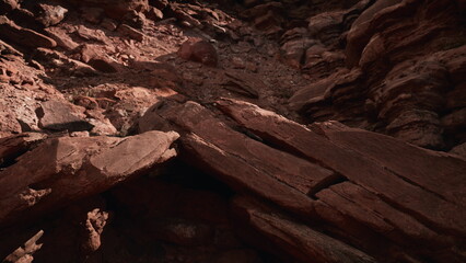 Sunlight filters softly over rugged red rocks and gravel on a desert floor. The ground showcases various textures and earthy tones, revealing natures beauty in a remote landscape.