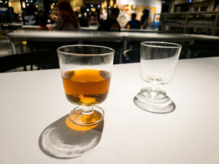 Close-up detail of a warm tea or herbal drink in a glass cup on a white table. Natural light creates dramatic shadows, suitable for themes of break, relaxation, or cafe culture