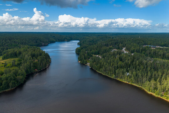 Aerial view of a dark lake reflecting the sky, surrounded by a dense forest, a serene contrast of water and foliage, Espoo, Uusimaa, Finland.