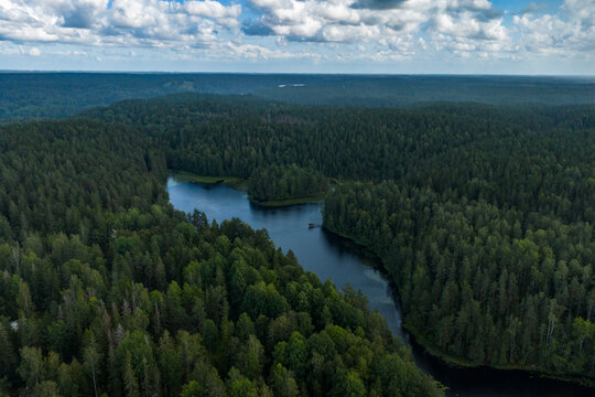 Aerial view of a winding river cuts through a dense forest, reflecting the sky's soft blues amidst the deep greens, Nuuksiontie, Espoo, Uusimaa, Finland.