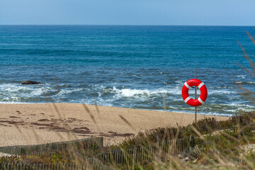 A red and white lifebuoy stands on a post overlooking a sandy beach
