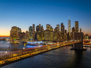 Aerial view of the Brooklyn Bridge stretching towards the illuminated skyscrapers and the One World Trade Center under the twilight sky, Manhattan, New York, United States.