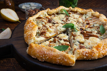 Homemade pear brie galette on wooden board, golden crust, melted cheese, honey glaze. Sliced galette with pear and bri cheese
