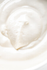 A close-up, high-angle shot of a smooth white creamy texture with soft swirls and gentle shadows. It could be cosmetic cream, yogurt, or dessert.