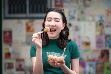 Young woman eating shumai street food with an excited expression, showing Asian cuisine, casual lifestyle, fun food experience, culture, candid emotion and tasty urban snack outdoors