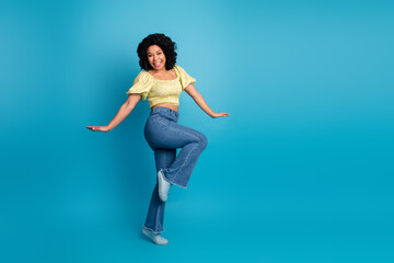 Obraz premium Young cheerful woman in casual attire striking a creative pose against a vibrant blue background