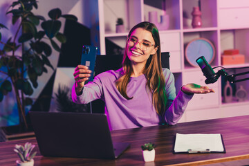 Charming female blogger hosting a live video session in vibrant neon lighting with microphone and...