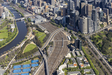 Aerial view of the Yarra River flowing through the heart of the city, with sunlight glinting off modern skyscrapers and railway tracks stretching towards the horizon, Melbourne, Victoria, Australia.
