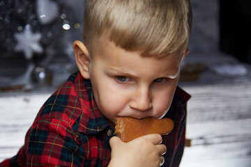 Adorable caucasian kid eats gingerbread and makes a funny face expression. Christmas food. Atmospheric, aesthetic Christmas home for New Year's Eve. Cheerful baby boy. Joyful, good mood.