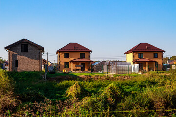 Modern suburban homes with vibrant gardens and greenhouses under a clear blue sky, hinting at tranquil country living