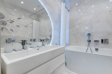 This sleek bathroom showcases a minimalist design with a freestanding bathtub, modern sink fixtures, and a well-lit mirror. The space is bright and inviting, perfect for relaxation.