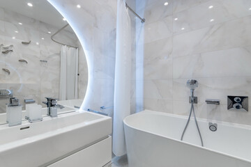 A spacious bathroom features a freestanding tub, modern sink, and stylish fixtures. Soft lighting enhances the clean design, creating a serene atmosphere for relaxation.