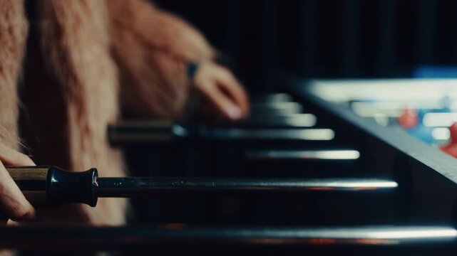 Unrecognizable woman wearing a faux fur coat enthusiastically playing a game of foosball in a dark room