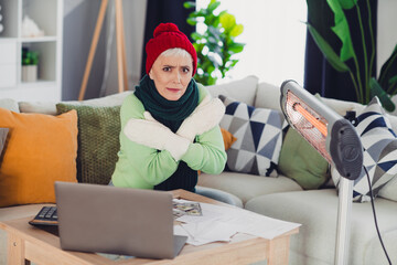 Senior woman in cozy home attire looking warmly near heater while working indoors, maintaining...