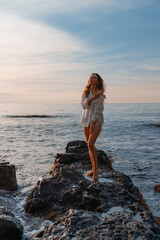 Woman sunrise ocean relaxing barefoot on rocky coastline enjoying golden morning light and freedom