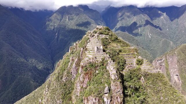 A dynamic shot circles the steep peak of Huayna Picchu at Machu Picchu, revealing the ancient stone stairs leading to the summit and the intricate structures and terraces built into its cliffsides