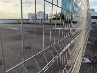 Metal wire fence in focus with blurred urban buildings in the background. Concept of security, restriction, boundary, and separation in modern city environment.