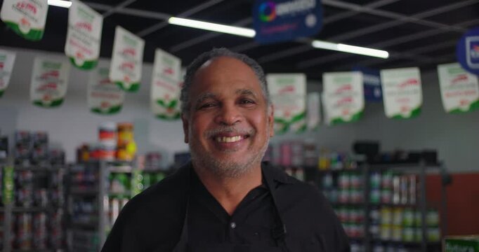 Cheerful small business owner smiling brightly in his hardware store, shelves of paint cans and banners in the background, creating a positive and welcoming atmosphere