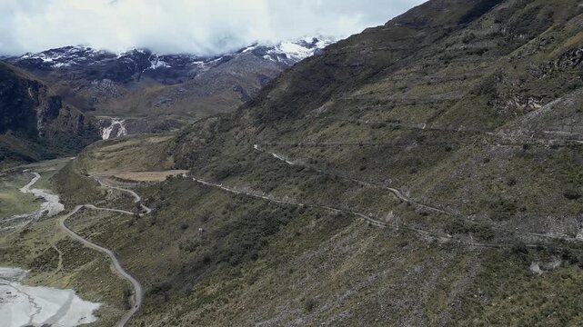 Huaraz, Peru: Drone footage of valley on the road to Punta Olimpica in Huascaran National Park in Peru showing snowcapped mountain in the background. Taken with rotation motion on cloudy day.