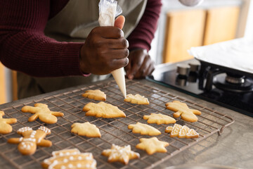 Piping bag tracing white icing on leaf and star cookies on cooling rack near gas stove