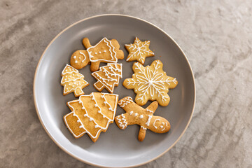 Round grey plate holding iced gingerbread people, tree and snowflake cookies on marble countertop