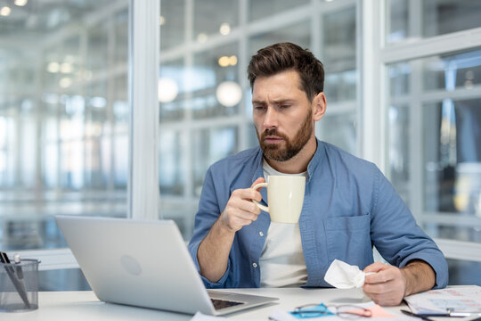 Businessman looking concerned while holding a coffee mug and crumpled paper, feeling stressed from work and experiencing burnout in a modern office environment