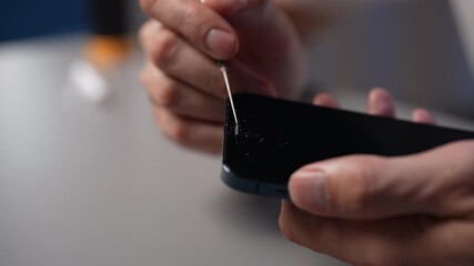 Professional technician cleaning smartphone device with a precision needle, removing dust and debris from the speaker grill, performing careful maintenance to optimize mobile phone performance