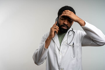 Stressed African American doctor talking on phone, holding head, isolated with copy space, healthcare concept