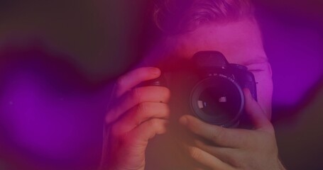 Photographer holding DSLR camera peering through viewfinder in studio, with purple red bokeh lights