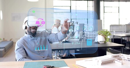 Gesturing man wearing grey shirt and VR headset at office desk, with gloves and data interface