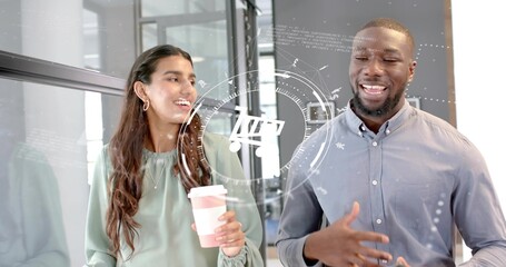 Walking Indian woman and colleague talking through glass corridor holding disposable coffee cup