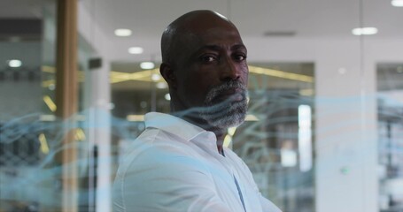 Standing executive wearing shirt viewing office through glass partition with printed blue graphics