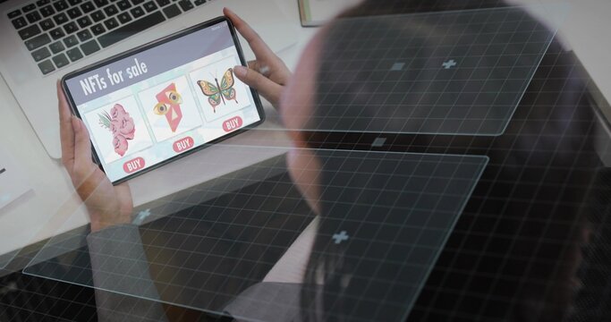 Browsing woman wearing gray top holding tablet showing NFT listings at desk with laptop, copy space - Powered by Adobe