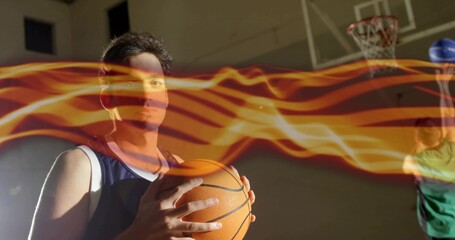 Holding basketball, player wearing blue jersey in gym, with hoop and flame light trails, copy space
