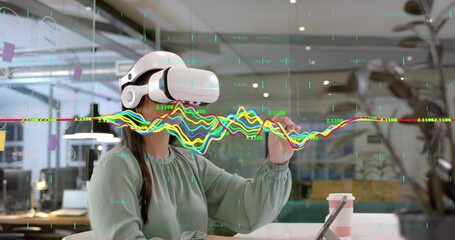 Using VR headset, woman wearing blouse exploring holographic data in office, with tablet and coffee