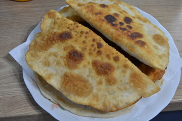 A close-up of golden, crispy fried pastries on a plate. Homemade deep-fried turnovers, possibly chebureki, with a bubbly, appetizing crust