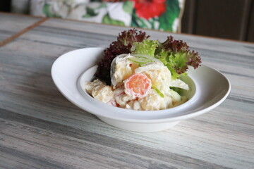 A fresh potato salad in a white bowl with green lettuce, a healthy appetizer