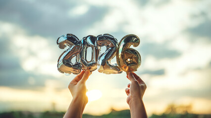Hands holding golden balloon numbers 2026 with sunset light, happy new year celebration and future concept, hope and success idea for holiday greeting and new beginning with warm golden atmosphere