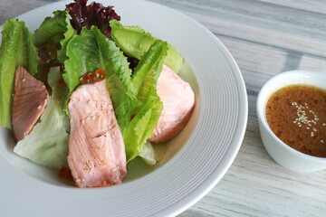 A delicious salmon salad served on a white plate with sauce in small bowl