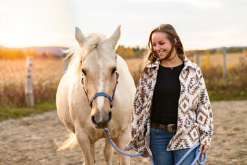 Fototapeta premium Young woman having great time with a horse in field on autumn season. sunset hour