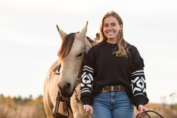 Young woman having great time with a horse in field on autumn season. sunset hour