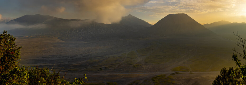 View of rugged volcanic peaks rise majestically under a warm golden light, casting long shadows across the desolate landscape, Bromo, East Java, Indonesia.