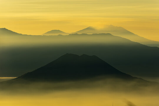 View of ethereal mountain peaks pierce through a sea of golden mist, bathed in the soft light of dawn, creating a serene landscape, Bromo, East Java, Indonesia.