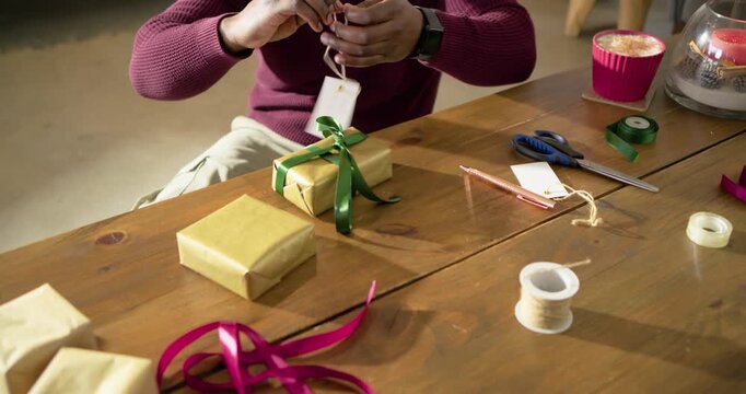 Inspired by holiday cheer, African American man tying green ribbon to gold gift box at home