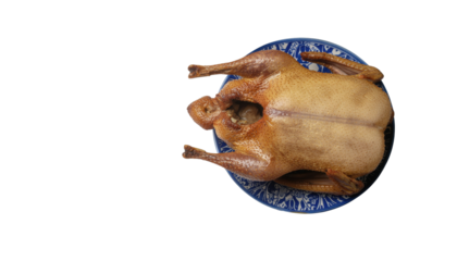 Roasted whole duck with golden brown skin presented on a blue patterned plate, top view on transparent background