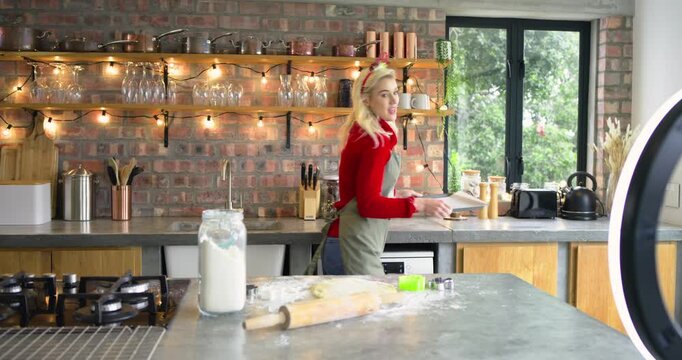 Woman wearing festive headband and apron showing star cutter dusting dough rolling cutting cookies