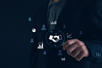 Digital business partnership and collaboration concept. A businessman pointing at handshake icon with data analytics graphics, representing corporate connection, teamwork, and technology innovation.